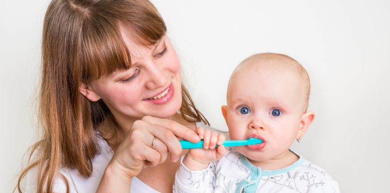 Mother brushing toddler's teeth with a blue toothbrush, emphasizing pediatric dental care and early oral hygiene education.